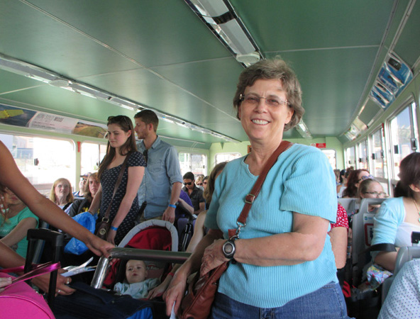 3 Photos show Dona sitting or standing in a boat with about 10 rows of 3 seats on each side of an aisle, and windows looking out onto the canal.