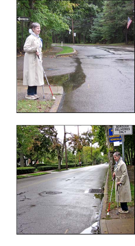 Two photos show Sue wearing a rain coat and holding a long white cane while standing at the corner of two 2-lane streets.  The first photo shows the street she is facing continue to her left and then disappear around a corner, the second photo shows the street to her right continue straight for at least a block, with a bus stop sign beside her.