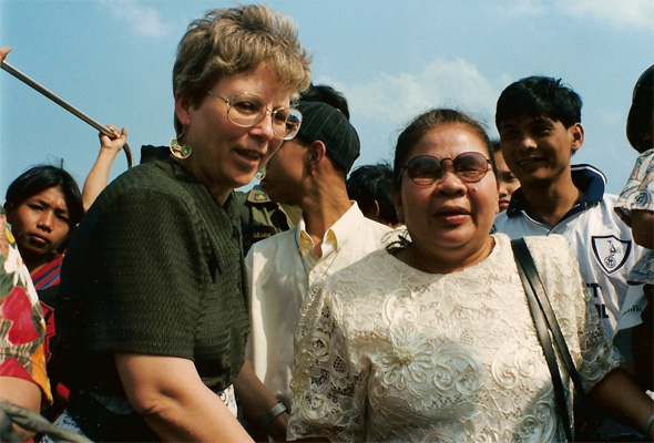 Photo shows the same crowd on the boat, but Nanta is now turned around and facing the camera, starting to smile and say something, and Dona has turned around and is leaning toward the front of Nanta, saying something.