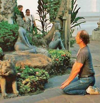 David sits on his knees in front of a small statue of a goddess serenely sitting on her knees. In the background are the sillouettes of Dona and Nanta.