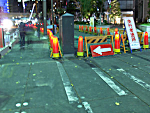 orange cones are placed in a street along some construction:  they appear to have a lightbulb inside the top.
