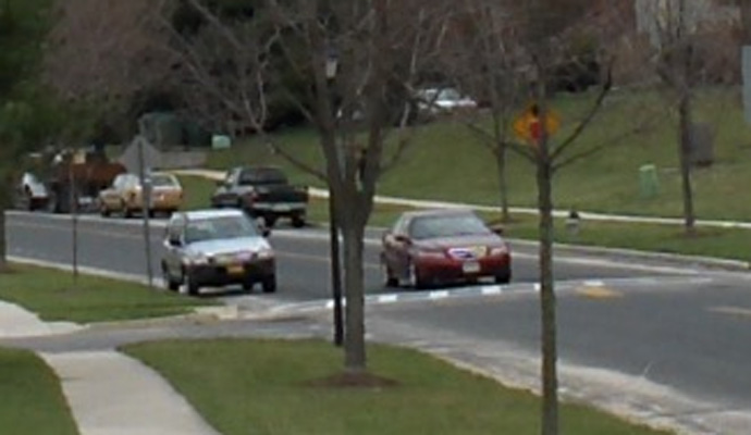 photo shows close-up of the speed hump, which extends across the street. A car approaches it and starts to ride over the hump.