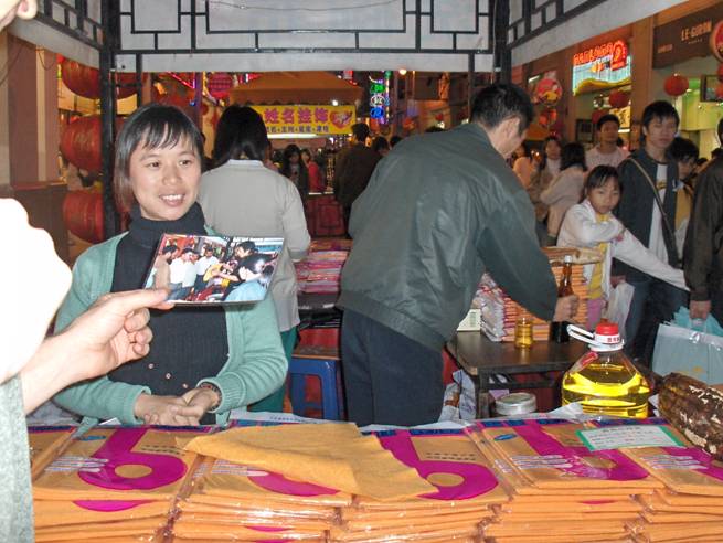 a woman inside the booth shows us a photo of herself and a man showing cloths to three Caucasian men with dark hair.