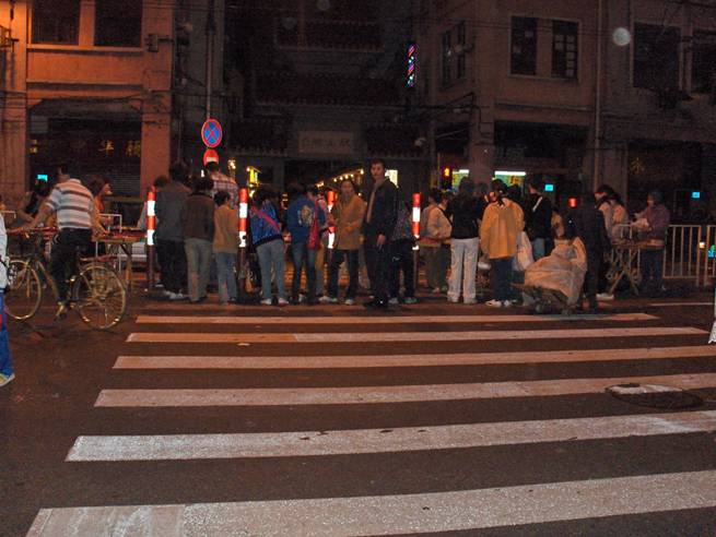 photo shows a crosswalk about 3 lanes to the middle. The middle is completely blocked with people standing around or looking at several tables.