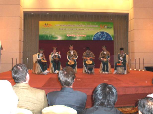 sitting on the stage are 6 children with drums and percussion instruments.