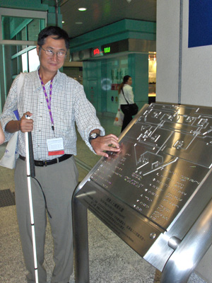 3 photos show people looking at a metal map about 2'x3' slanted like a lecturn.  The map has a braille legend and raised lines and symbols.