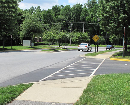 Photo shows a crosswalk across a narrow two-lane street or entrance, intersecting Donaldson Street on our left.  Donaldson has two wide lanes and a grassy median strip.