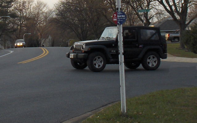 Photo shows a jeep starting to turn left into a 2-lane street.  A car is approaching the intersection from about 40 feet to the jeep's right.