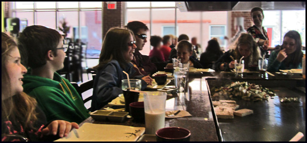 The students sit around the table with the grill in the middle.