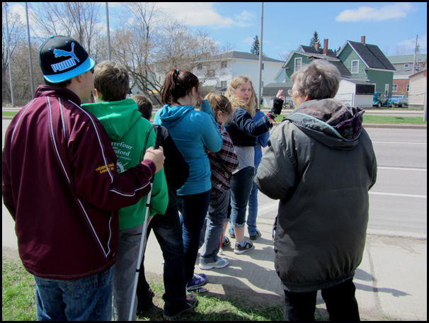 Both photos show the students lined up to face the street and listen to the traffic, with instructors standing beside the line.