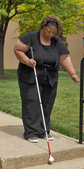 The woman has moved a little closer to the edge and leaned forward even more, looking down.