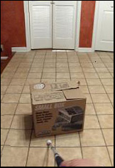 picture shows a floor below and a door and wall ahead; in the bottom of the photo we can see a hand holding a cane extended forward almost reaching a small box (about 2 feet high and wide).