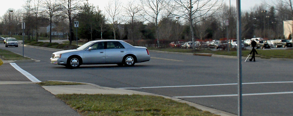 Photo shows a car crossing a 3-lane street from a stop sign.  A stick figure crosses beside it, and to the figure's right is a car approaching from about 30 feet away.