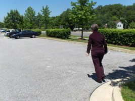 4 photos show Dona stepping off a curb in the parking lot and walking across about 7 parking spaces, then standing at one of the lane markers for the parking spaces.
